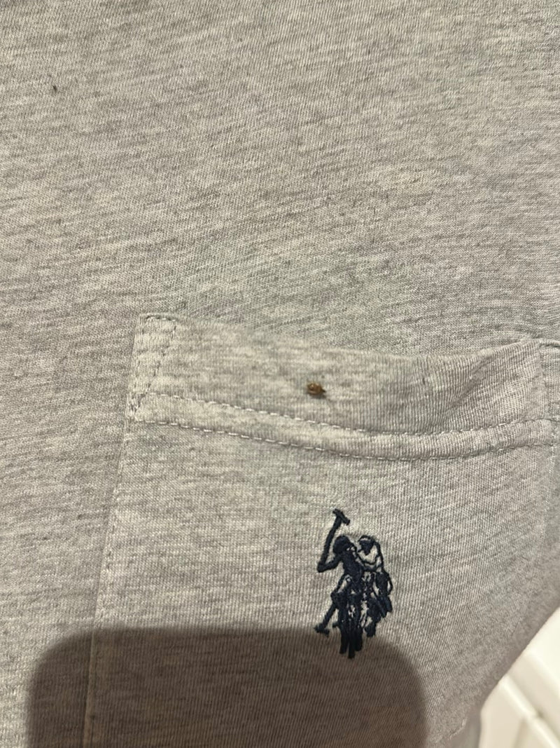 Een kleine bedwants zit op een grijze textielstof met een zak. Het insect is erg klein en nauwelijks herkenbaar.