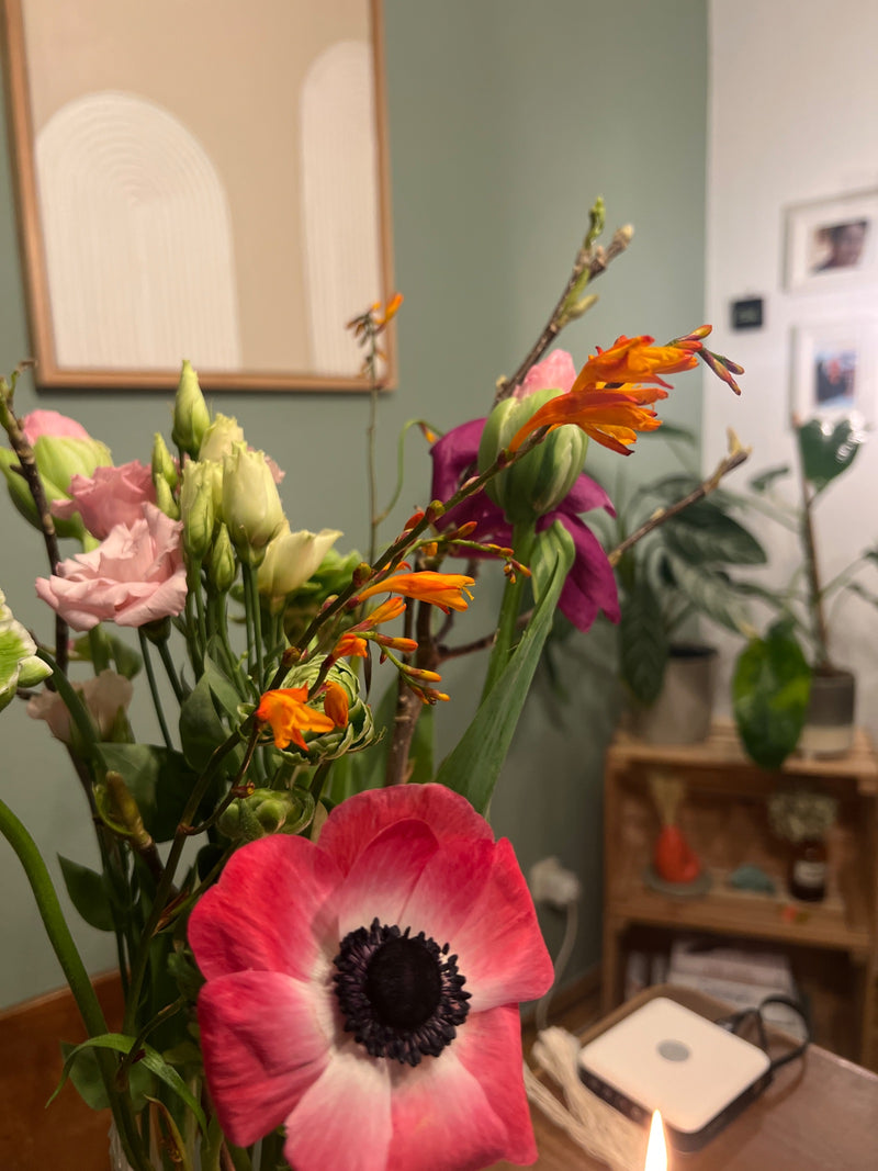 Op de voorgrond is de geopende bloem van een oosterse anemoon met roze-witte bloemblaadjes en een donker hart te zien. Deze maakt deel uit van een boeket sni...