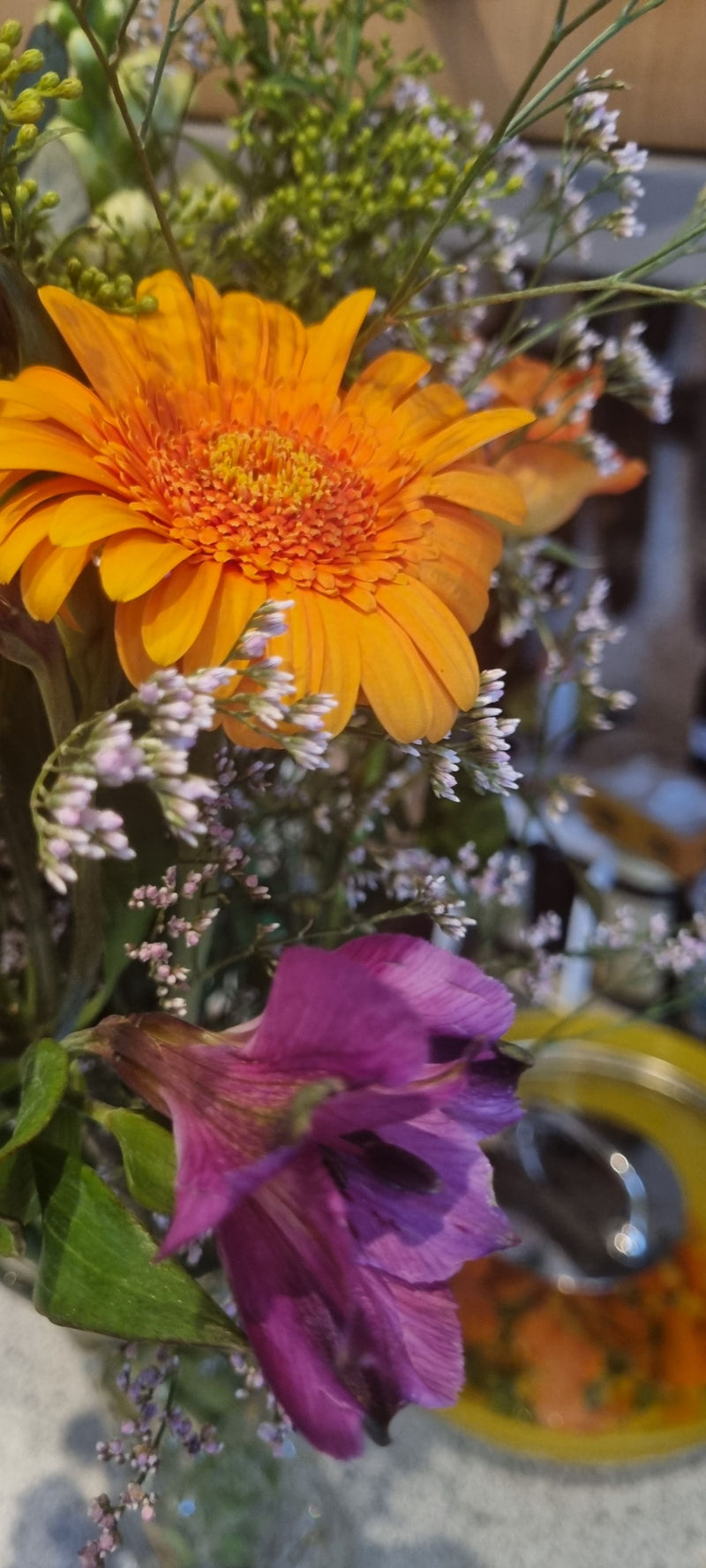 Te zien is een felle oranje gerbera als onderdeel van een kleurrijk boeket. De kenmerkende bloembladeren en het hoofdjesbloemweefsel zijn goed zichtbaar.