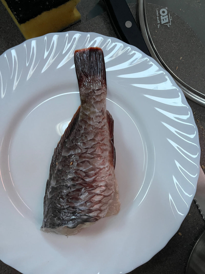 Een stuk karper met duidelijke schubben en de staartvin ligt op een wit bord.