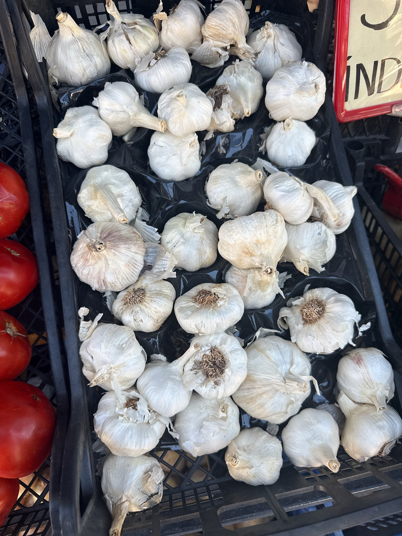 De afbeelding toont talrijke witte knoflookbollen dicht op elkaar in een zwarte verkoopkist op een markt.