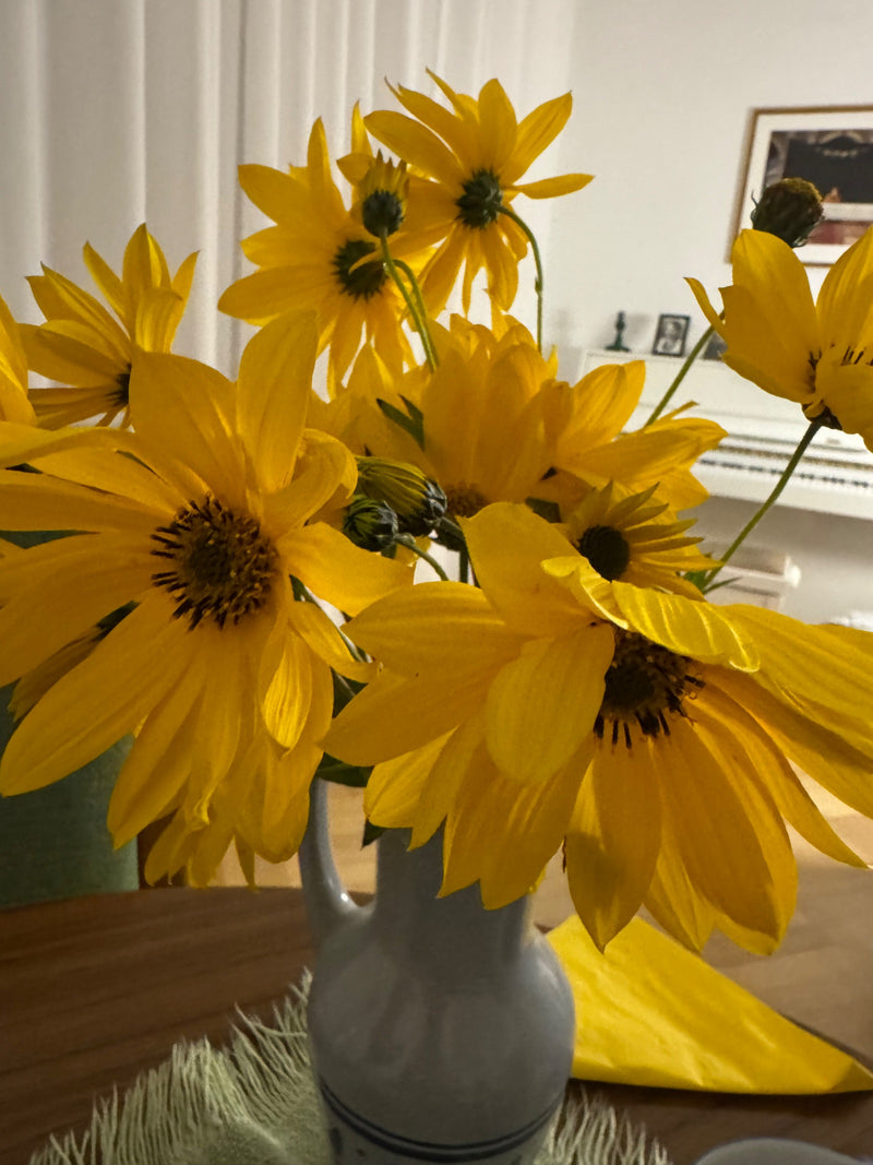 Een boeket felgele aardpeerbloemen staat decoratief in een lichte keramieken vaas op een tafel binnenshuis.
